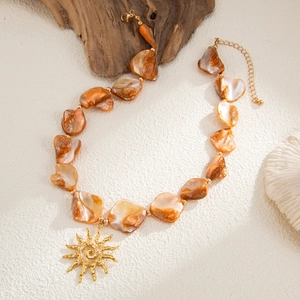 Detail of bohemian beaded necklace featuring orange natural beads and gold sun pendant