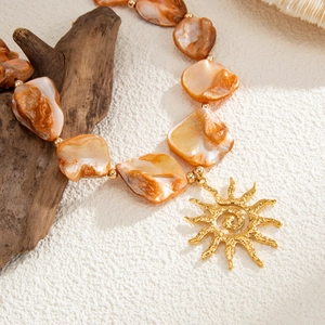 Close-up of bohemian necklace with orange shell-like beads and a gold sun pendant charm