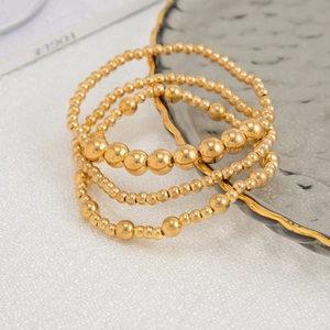 Nahaufnahme eines 4-teiligen Goldperlenarmband-Sets auf einem eleganten Glaswellenteller