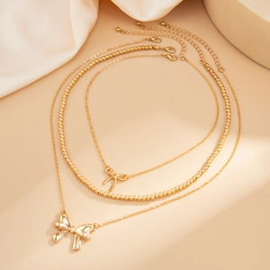 Three-layer gold bow necklace with bead chain and layered pendants on silk background