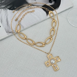 Details einer mehrlagigen Goldhalskette mit Perlenkreuz an einer groben Gliederkette