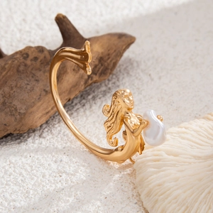 Détail d'un ear cuff sirène doré avec perle baroque sur un fond de sable texturé