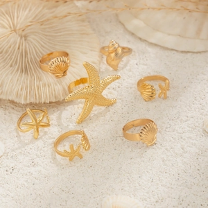 Makroaufnahme goldener Strandringe mit Seestern- und Muschelmotiven auf Sandhintergrund