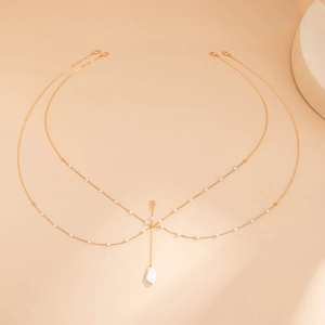 Detail of layered gold body chain featuring white pearls and a baroque pearl drop charm