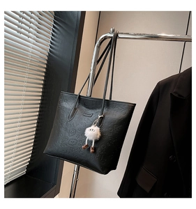 Detail of black tote bag featuring embossed cartoon motifs and white plush charm