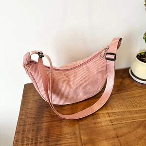 Pink corduroy crescent crossbody bag with adjustable strap on a rustic wooden table