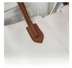 Close-up of contrast stitching on creamy tote bag with brown leather handle texture