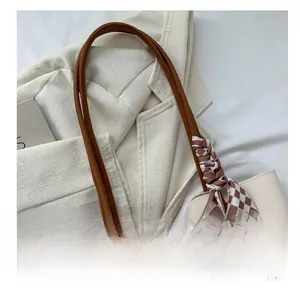 Detail of beige tote bag with brown leather handles and checkered silk scarf accessory