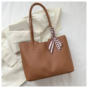 Close-up of brown faux leather tote bag with decorative scarf on a white blazer