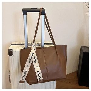 Détail d'un sac cabas marron en similicuir avec ruban décoratif sur une valise