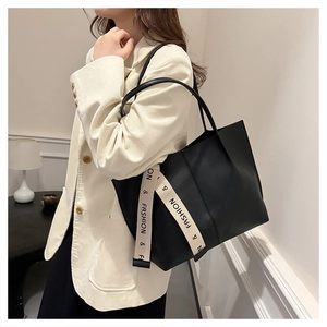Détail d'un sac cabas noir en cuir avec des lanières tissées blanches au style tendance