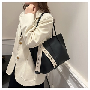 Détail du grand sac cabas noir avec ruban mode porté par une femme en veste beige