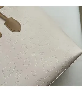 Detail of off-white tote bag featuring cartoon embossed pattern and brown leather handle