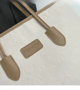 Detail shot of beige faux leather tote showing embossed cartoon patterns and logo