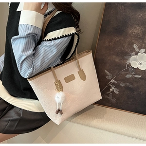 Detailed macro view of the cream tote bag with embossed cartoon patterns and plush charm