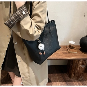 Detail of black tote bag featuring embossed logo textures and a plush character charm