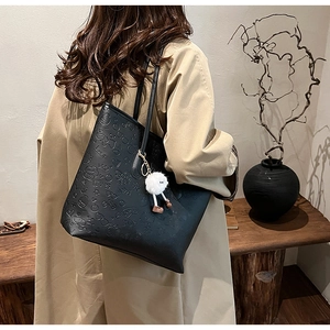 Close-up of black tote bag with embossed heart patterns and white fur ball charm