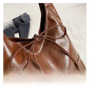 Detail of dark brown tote bag featuring glossy oil-wax texture and a ribbon bow knot
