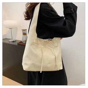 Close-up of beige hobo bag detail featuring a soft faux leather texture and a delicate bow tie