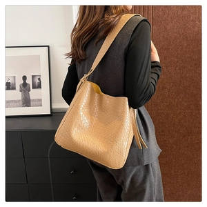 Detail of caramel woven tote bag with wide shoulder strap worn by model in home setting
