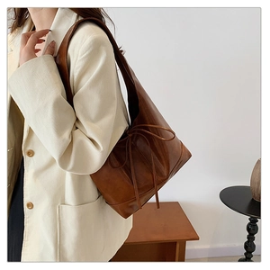 Brown leather underarm bag with drawstring detail shown on a model in a corduroy jacket