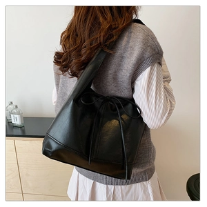 Detail of black PU leather tote bag featuring a decorative drawstring bow and soft texture