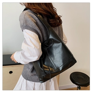 Close-up of minimalist black PU leather underarm bag with side drawstring bow detail