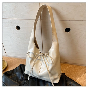 Detail of off-white PU leather hobo bag with an elegant ribbon bow on a dark background