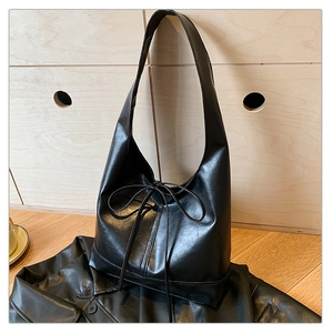 Close-up of black leather hobo bag with slim drawstring bow detail on a leather jacket