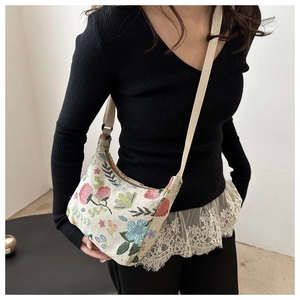 Détail d'un sac bandoulière en toile fleurie avec fleurs roses et sangle beige sur modèle