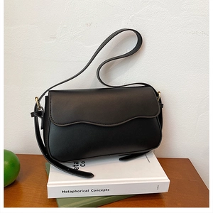 Detail of black leather underarm bag featuring wave edge flap and gold metal hardware buckle