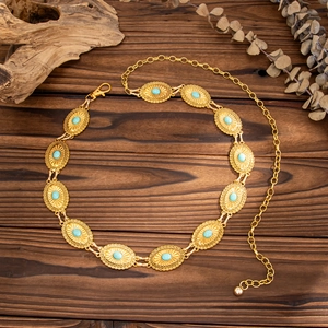 Detail of bohemian gold waist chain featuring turquoise inlays on a vintage wooden table