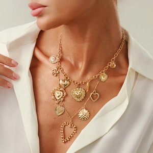 Detail of layered gold heart and sun medallion pendant necklace on a white shirt