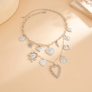 Detail of layered silver necklaces with heart, fish and sunflower pendants on beige stones