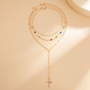 Dettaglio della collana dorata a strati con pietre colorate e ciondolo a croce