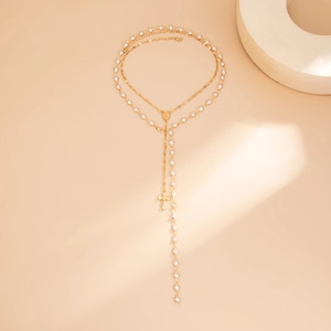 Dettaglio della collana a Y dorata con perle e ciondolo a croce su base di pietra