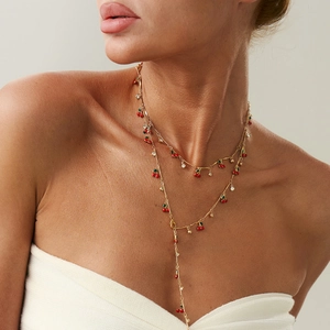 Dettaglio di una collana dorata a più strati con ciondoli a ciliegia rossa e cristalli