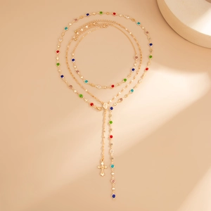 Dettaglio di una collana dorata a strati con perline colorate e ciondolo a croce