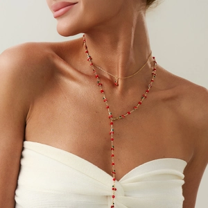 Dettaglio della collana a strati color oro con ciliegie rosse e foglie verdi indossata
