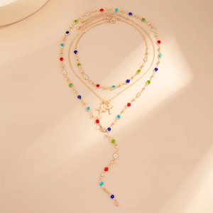 Dettaglio collana boho a tre strati dorata con gemme colorate e ciondoli a croce