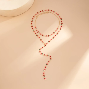 Dettaglio della collana a Y dorata con ciliegie di perline rosse e foglie verdi