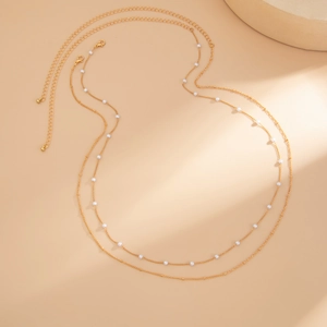 Dettaglio di una catena per il corpo a doppio strato dorata con eleganti perle bianche