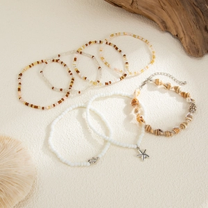 Flat lay of bohemian 7-piece anklet set with starfish and turtle charms and shells