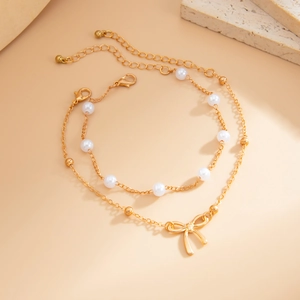 Close-up of double-layer gold anklet with white pearls, beads and delicate bow pendant