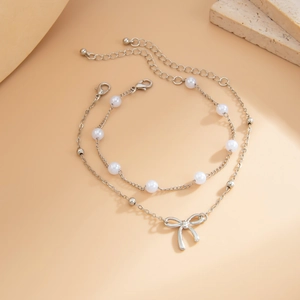 Detail of two-piece chain anklets with pearls and silver bow pendant on a soft background