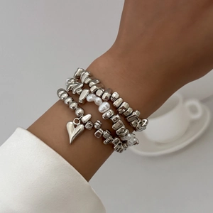 Detailed view of layered silver beaded bracelets with heart charm and baroque pearls