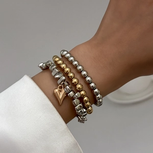 Close-up of a stacked bracelet set with silver and gold beads and a heart-shaped pendant