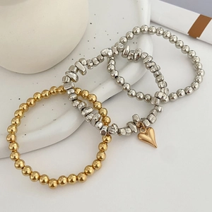 Close-up of three-piece beaded bracelet set featuring silver beads and a gold heart pendant