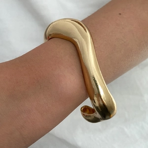 Dettaglio di un bracciale rigido dorato ondulato dal design geometrico minimalista unico