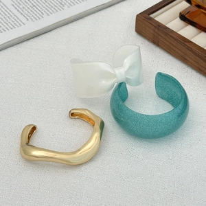 Dettagli di bracciali irregolari in metallo dorato, resina blu glitter e fiocco crema